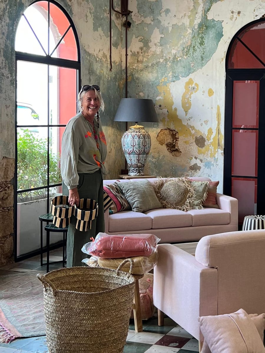 Smiling woman in the showroom holding two striped baskets, with a pink sofa and a patterned lamp behind her